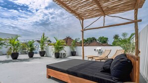 A rooftop bedroom with a wooden bed, lounge chairs, and potted plants. - Villa Tulum (Canggu)