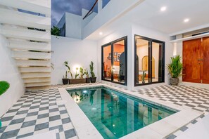 A modern pool area with a checkered floor, a glass-enclosed room, and a wooden door. - Villa Tulum (Canggu)