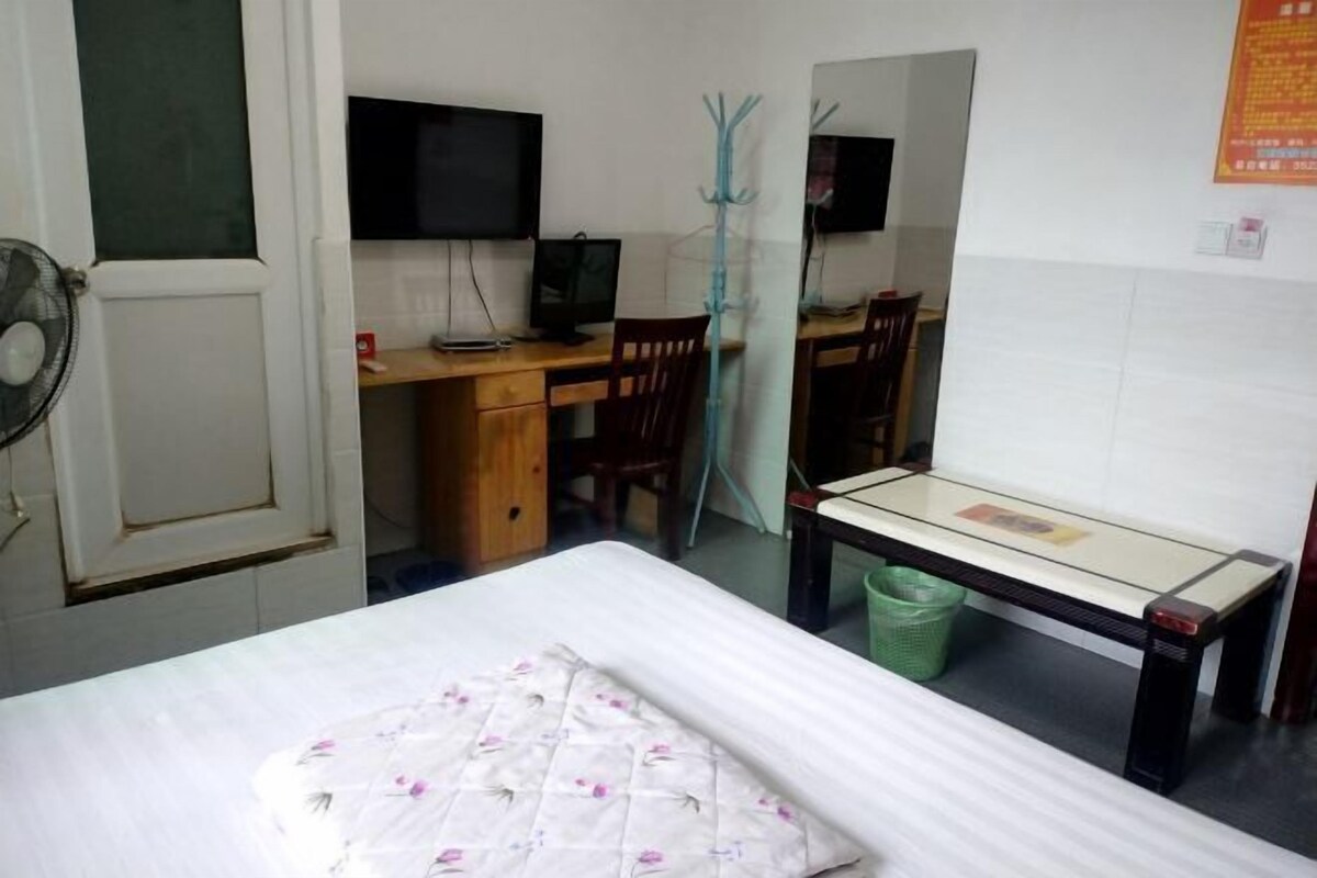 Un dormitorio con una cama, un escritorio con una computadora, una silla, un espejo y un ventilador.