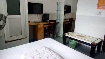 A bedroom with a bed, a desk with a computer, a chair, a mirror, and a fan.