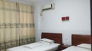 A hotel room with two beds, a wooden headboard, an air conditioning unit, and a curtain with a floral pattern. - Xinhua Huihong Hotel (Xinhua)