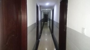 A long, narrow hallway with dark wooden doors on both sides and a shiny tiled floor. - Xinhua Huihong Hotel (Xinhua)