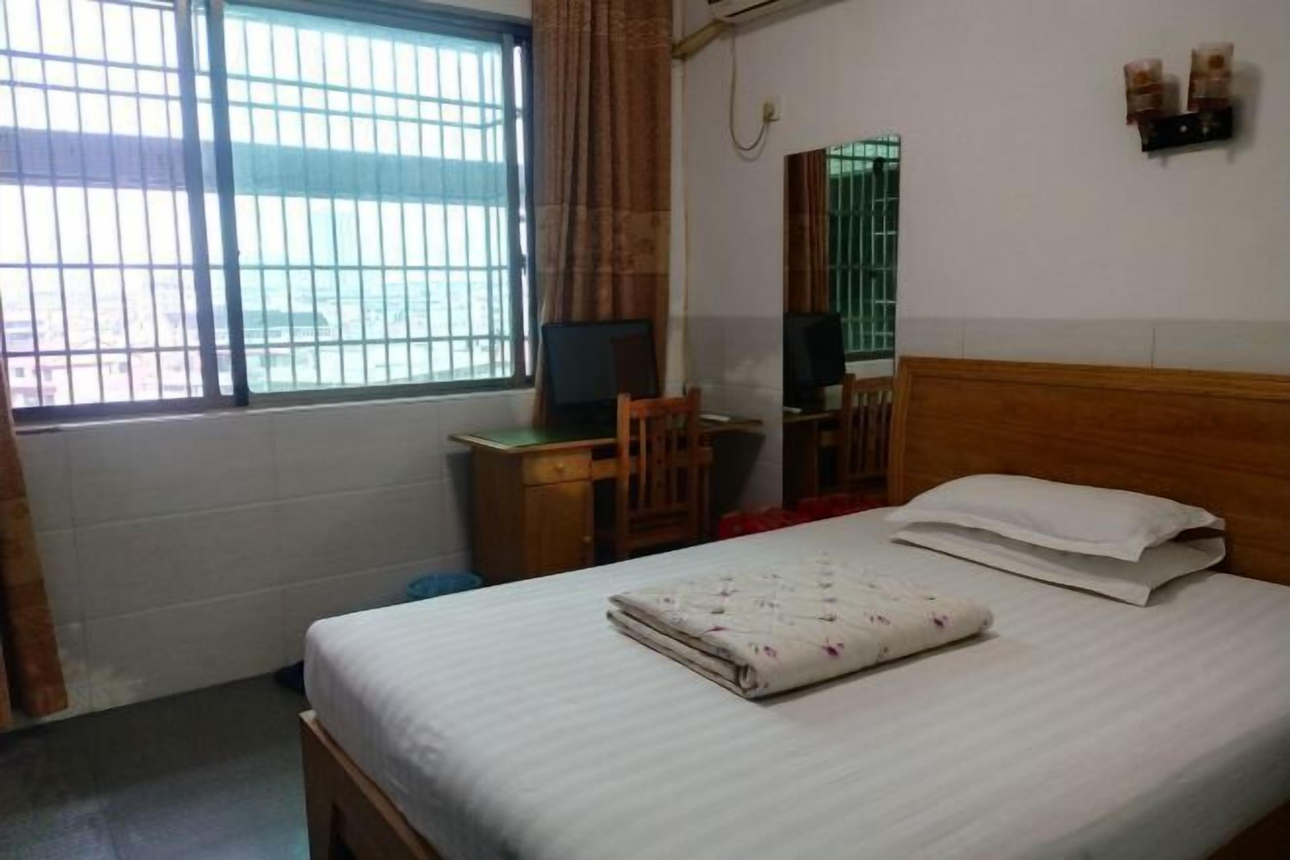 A hotel room with a bed, a desk, a chair, a mirror, and a window with bars.