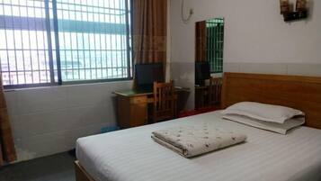 A hotel room with a bed, a desk, a chair, a mirror, and a window with bars.