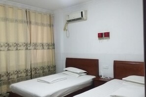 Una habitación de hotel con dos camas, un equipo de aire acondicionado y una cortina con estampado floral.