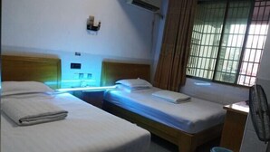A room with two single beds, a small table, a fan, and a window with curtains. - Xinhua Huihong Hotel (Xinhua)