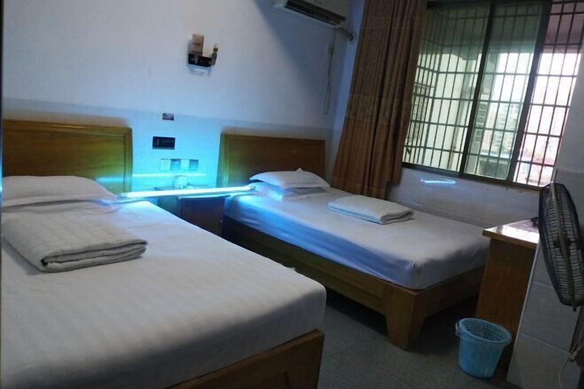 Una habitación con dos camas individuales, una mesita, un ventilador y una ventana con cortinas.
