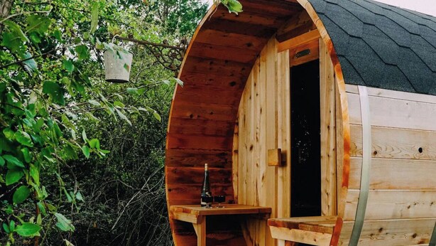 A wooden cabin with a curved roof, a small table with a bottle, and a bench inside. - 1 Bed Tiny House Sleeps 2 -Hot Tub -Coal Fireplace (Liglet)