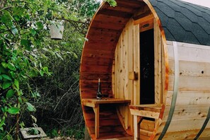 A wooden cabin with a curved roof, a small table with a bottle, and a bench inside. - 1 Bed Tiny House Sleeps 2 -Hot Tub -Coal Fireplace (Liglet)