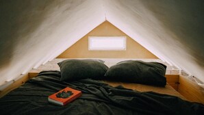 A small, triangular attic bedroom with a single bed, two pillows, and a book on the bed. - 1 Bed Tiny House Sleeps 2 -Hot Tub -Coal Fireplace (Liglet)