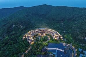 A large, circular hotel with multiple levels and a central courtyard, surrounded by dense forest and hills. - Wuxi Nianhua Bay Polomydo Hotel, (Wuxi)