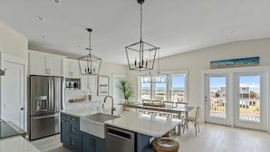 A modern kitchen with a central island, stainless steel appliances, and pendant lighting. - New!  Spectacular Ocean & Marsh Views, Elevator, Pool, Den, ADA, Steps to Beach! (Oak Island)