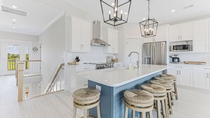 A modern kitchen with white cabinets, a blue island, and bar stools. - New!  Spectacular Ocean & Marsh Views, Elevator, Pool, Den, ADA, Steps to Beach! (Oak Island)