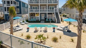 A two-story building with a pool, outdoor seating, and a fenced patio area. - New!  Spectacular Ocean & Marsh Views, Elevator, Pool, Den, ADA, Steps to Beach! (Oak Island)