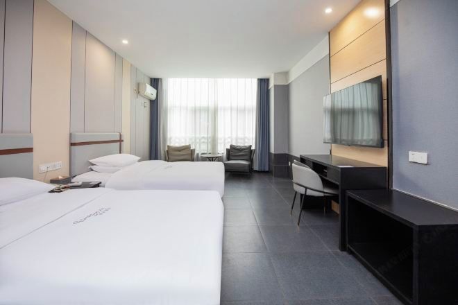 A hotel room with two beds, a desk, a chair, a TV, and a large window with curtains.
