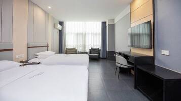 A hotel room with two beds, a desk, a chair, a TV, and a large window with curtains.