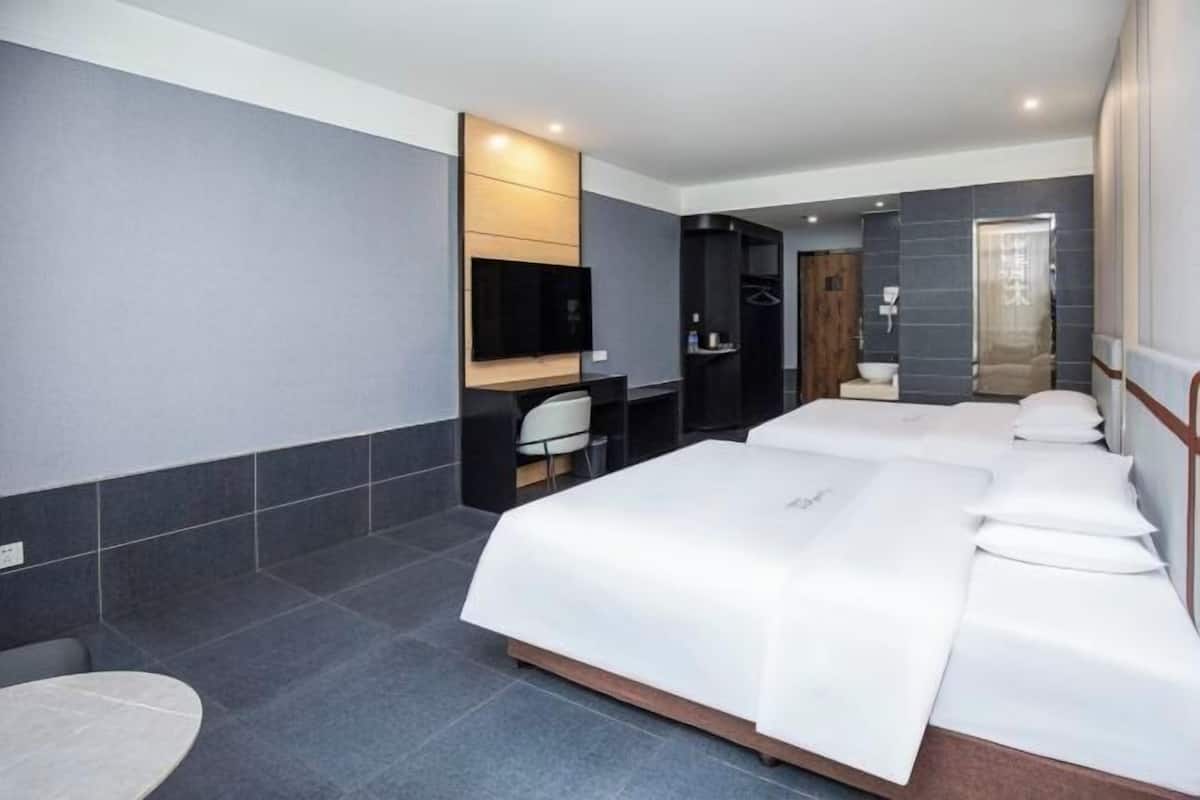 A hotel room with a large bed, a desk, a chair, a small table, and a shower area.