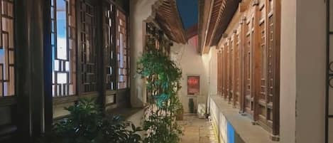 A narrow alleyway with traditional architecture, potted plants, and a signboard.