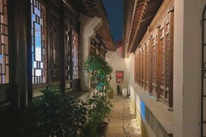 Uma viela estreita com arquitetura tradicional, plantas em vasos e uma placa.