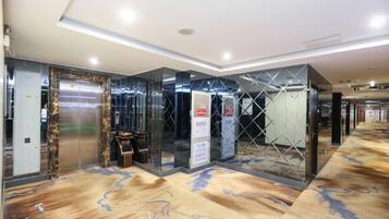 A hotel lobby with a marble floor, elevators, and a reception desk.
