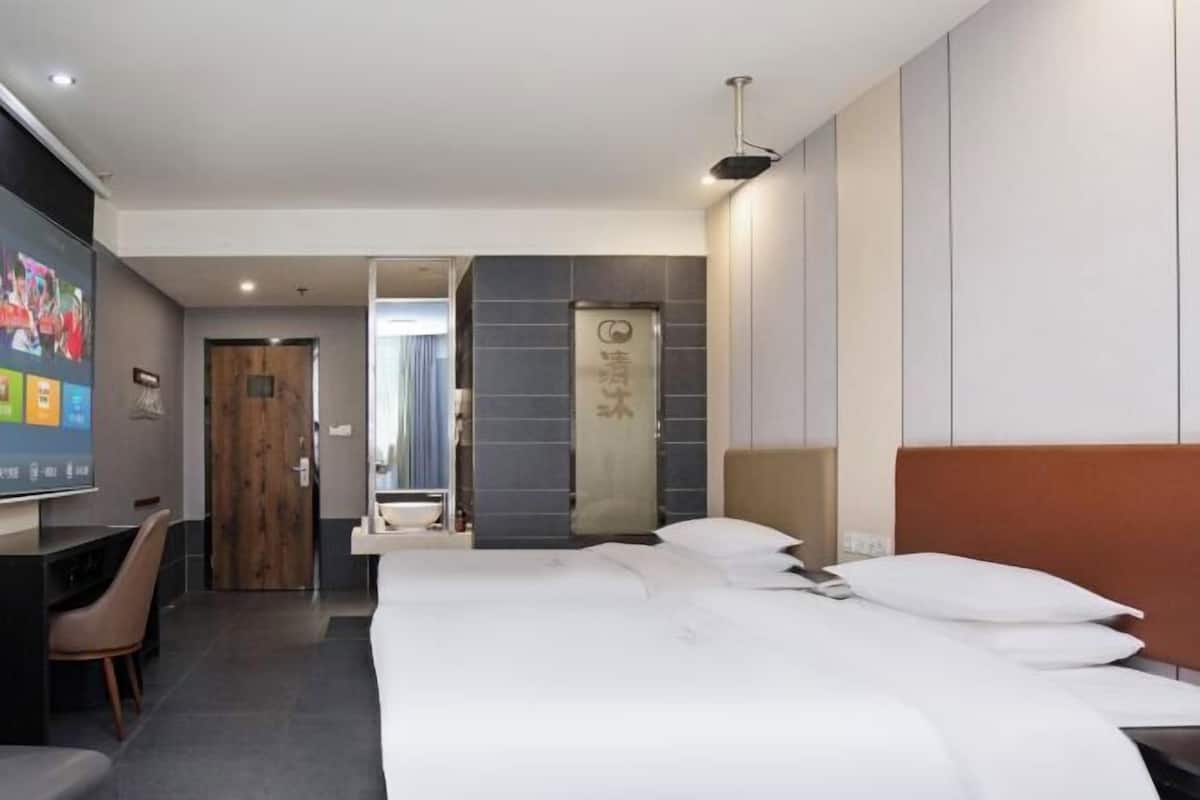 A hotel room with a bed, a desk, a chair, a TV, and a bathroom door.