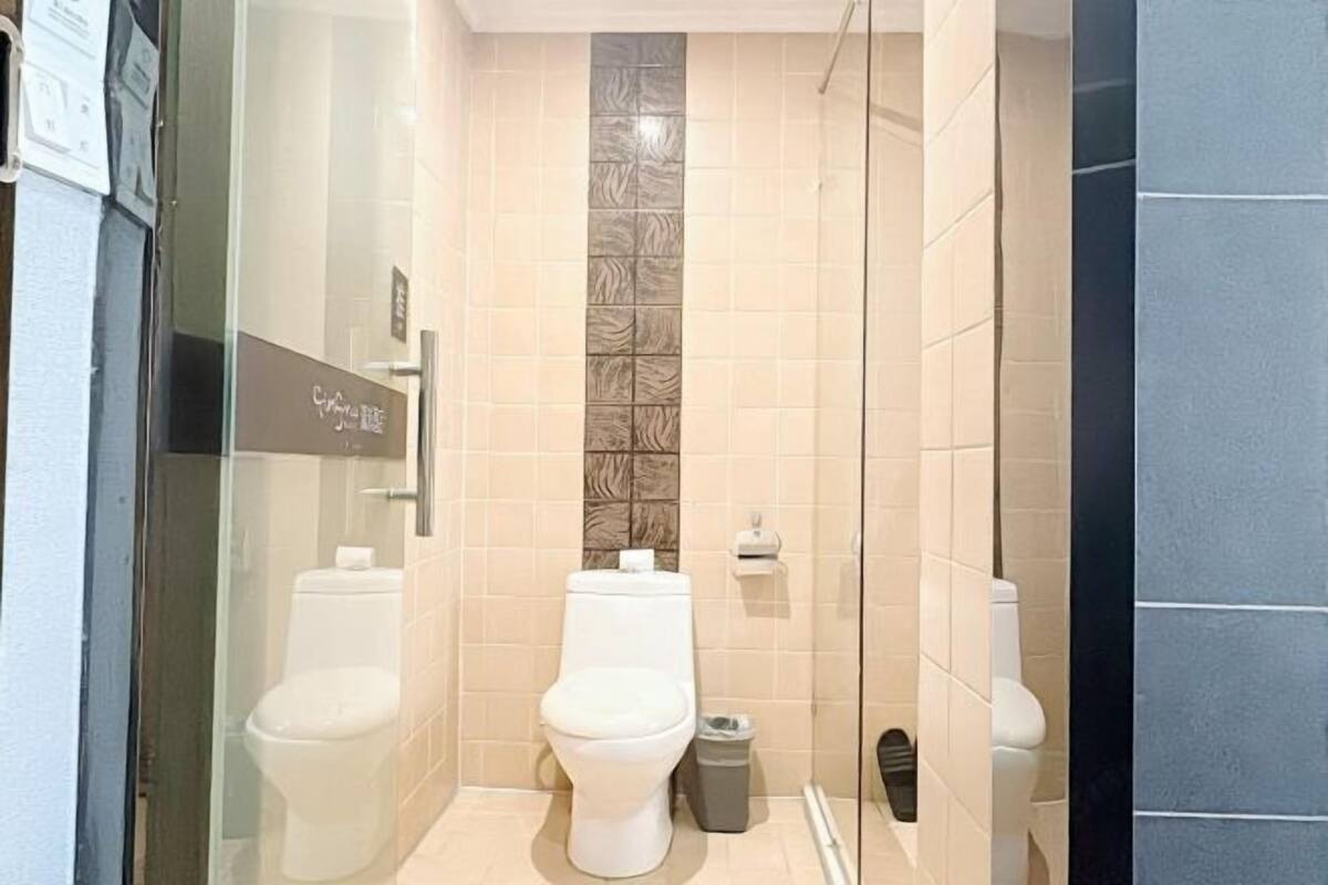 A bathroom with two toilets, a glass shower enclosure, and a tiled wall with a decorative pattern.