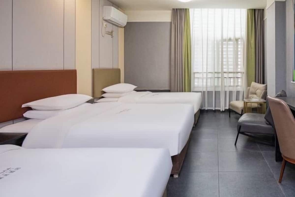 A hotel room with three beds, a seating area, and a window with curtains.