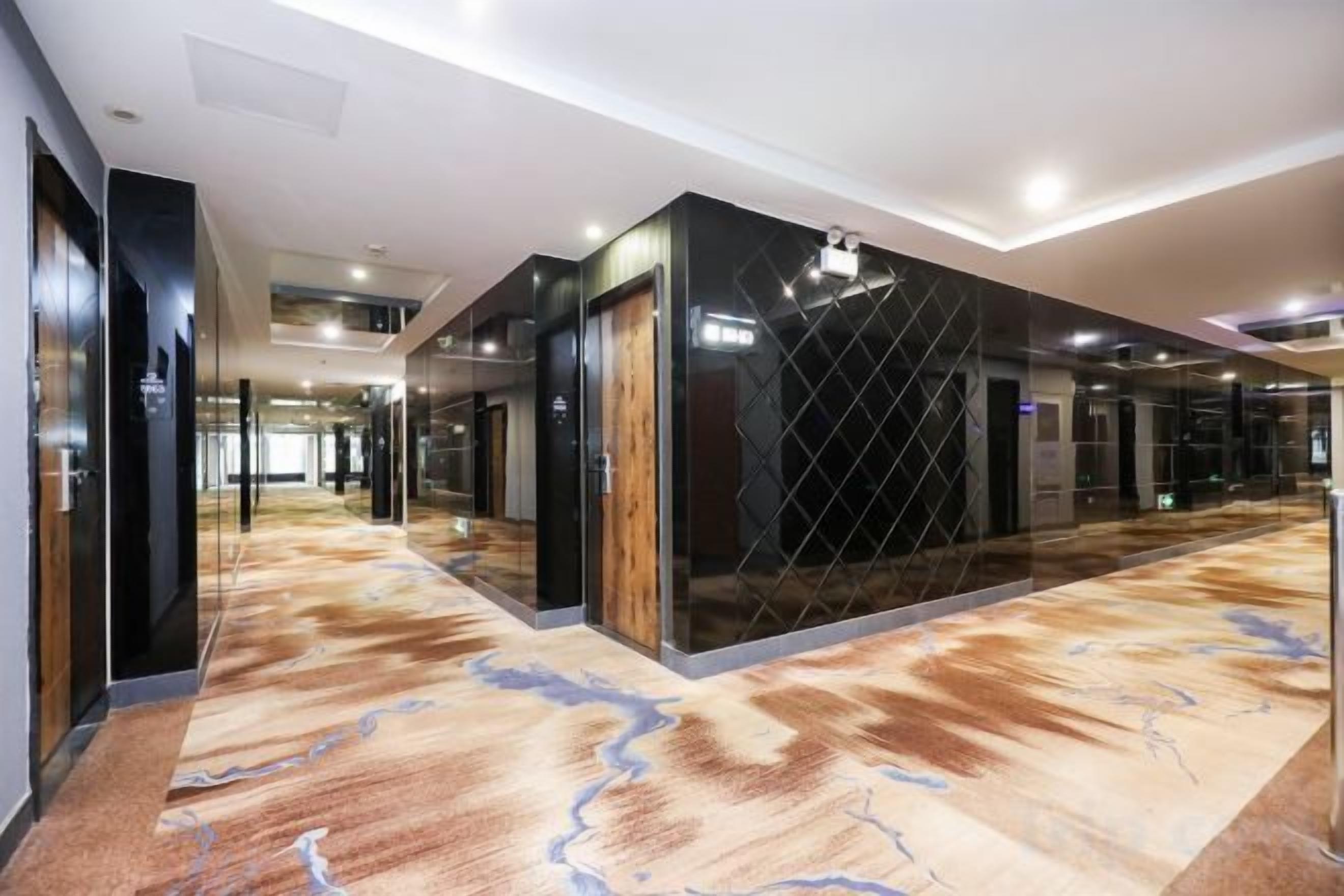 Un pasillo de hotel con alfombra estampada, paredes espejadas y un diseño moderno de techo.
