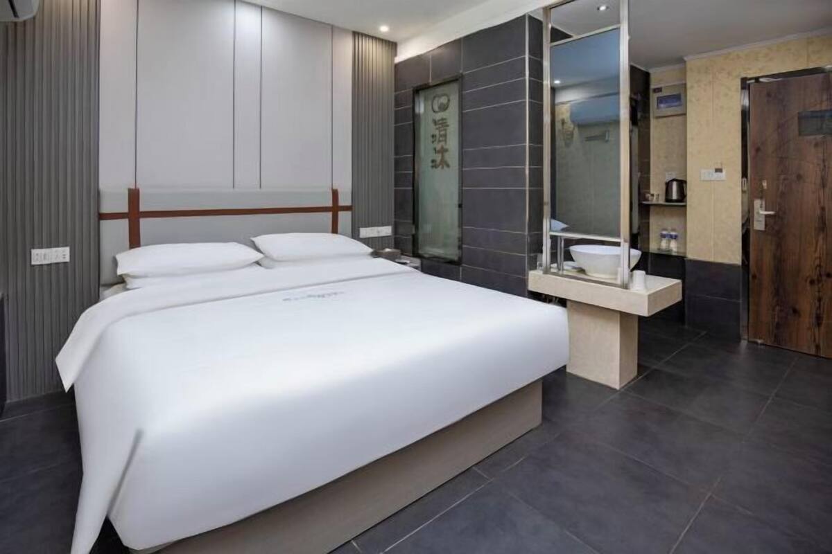 A modern hotel room with a large bed, a bedside table, a mirror, and a bathroom with a sink and toilet.