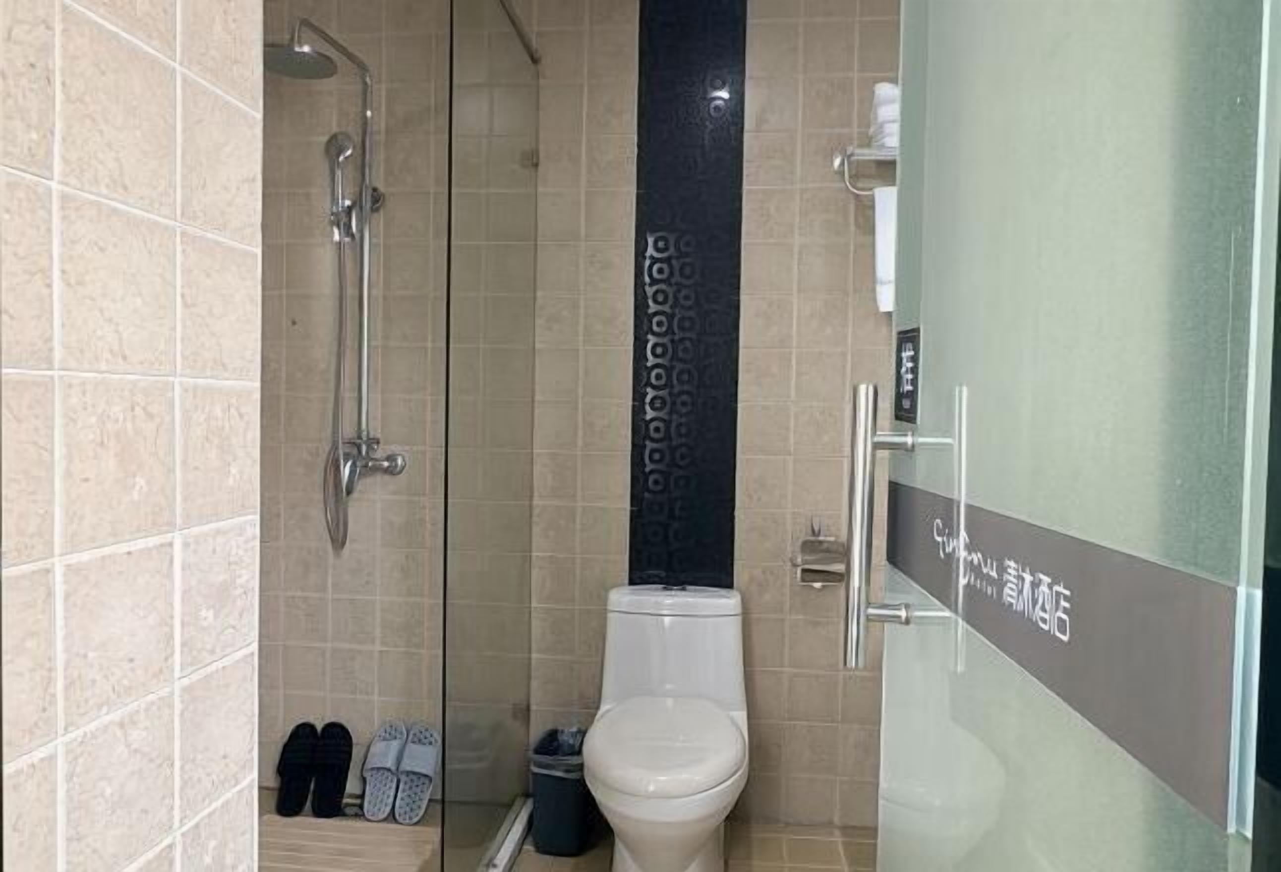 A bathroom with a shower, toilet, and a pair of slippers on the floor.