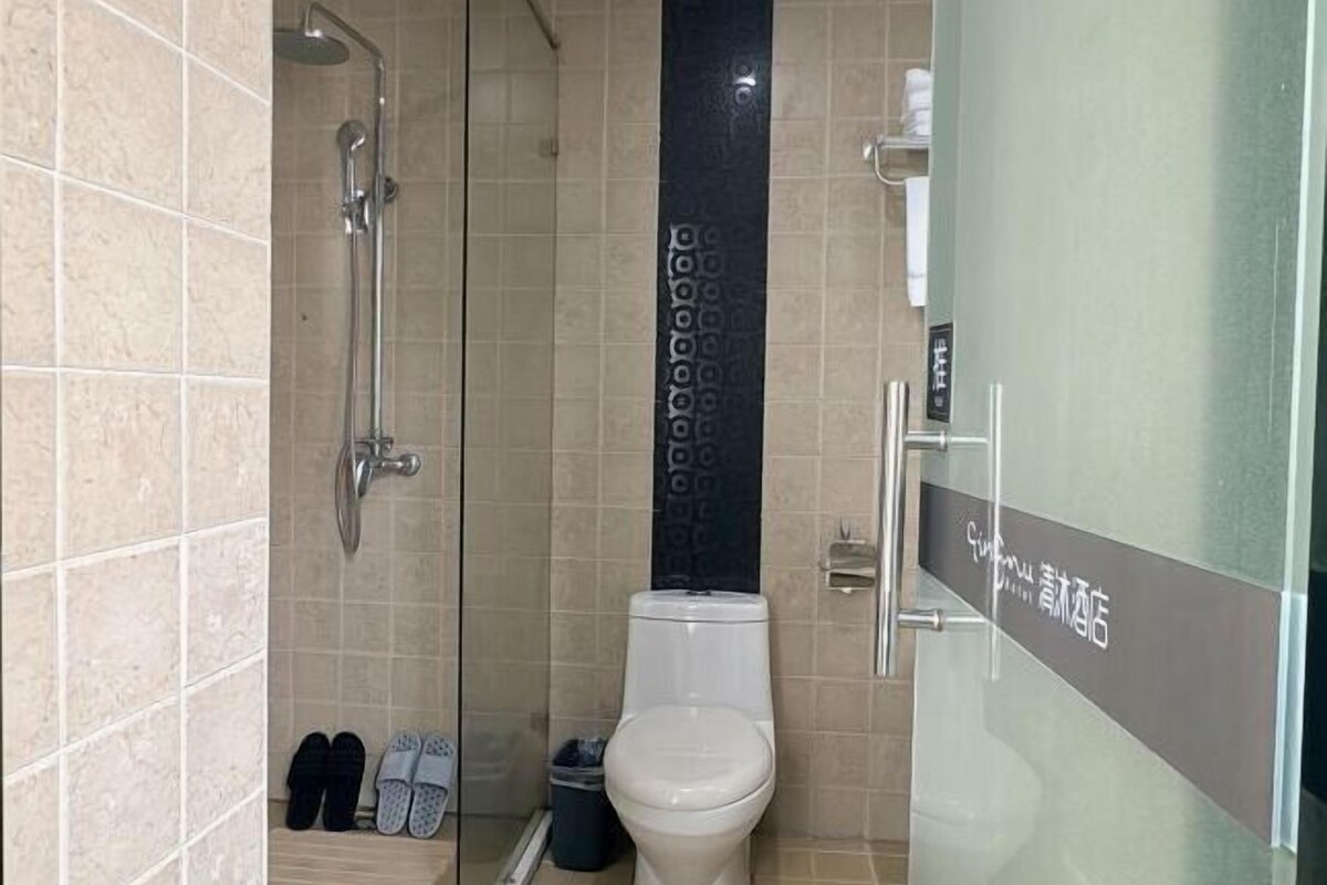 A bathroom with a shower, toilet, and a pair of slippers on the floor.