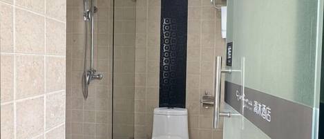 A bathroom with a shower, toilet, and a pair of slippers on the floor.