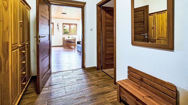 A hallway with wooden flooring, a bench, and a dining area with a table and chairs.