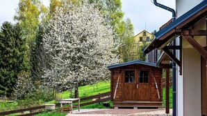 A wooden cabin with a brick pathway leading to it, surrounded by lush greenery and a large flowering tree.
