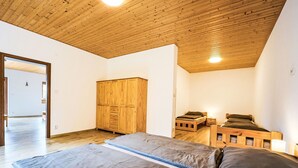 A room with a wooden ceiling, a wardrobe, a bed with a mattress and pillows, and a bedside table with a lamp.