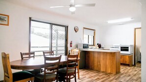A dining area with a wooden table and chairs, a kitchen with a microwave and stove, and a ceiling fan. - House 3 BR with parking, Close to hospital 2.2km Red Energy Arena Bendigo 1.6 km (Golden Square)