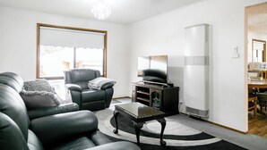 A living room with a black leather sofa, a black armchair, a glass coffee table, and a large window with a view of a building. - House 3 BR with parking, Close to hospital 2.2km Red Energy Arena Bendigo 1.6 km (Golden Square)
