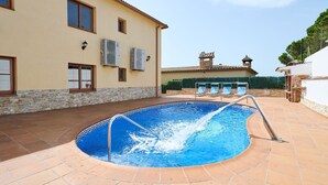 A swimming pool with a metal ladder, surrounded by a tiled patio, and a building with stone and brick walls in the background.