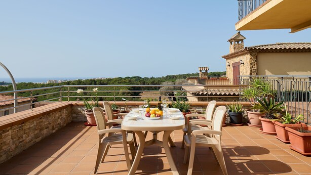 A terrace with a table set for two, surrounded by potted plants and a view of the city.