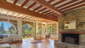 Amplia sala de estar con vigas de madera, chimenea de piedra y vistas al exterior.
