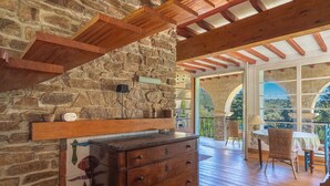 Una rústica pared de piedra con un estante de madera, un aparador de madera y vistas a un patio exterior con una mesa y sillas.