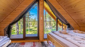 Une pièce triangulaire en bois, avec un lit, une fenêtre et une vue sur un paysage verdoyant.