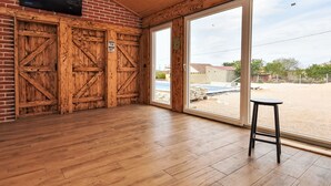 Ein geräumiger Raum mit Holzboden, einer großen Schiebeglastür, die zu einem Außenbereich führt, und einem an einer Backsteinwand befestigten Fernseher.