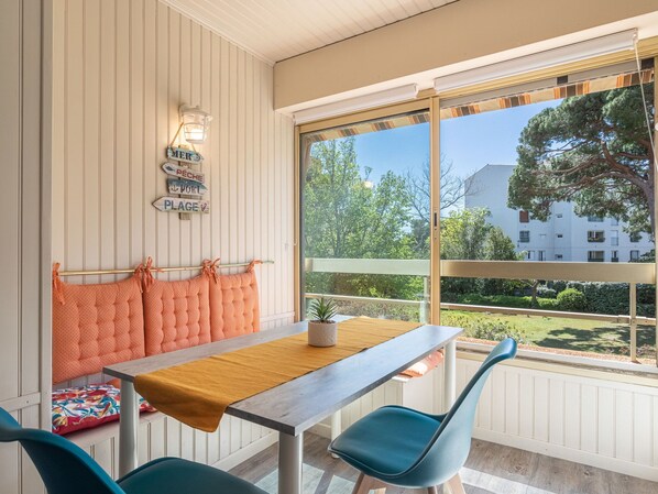 Enjoy a meal for two by the window with a view of lush greenery and a residential building.