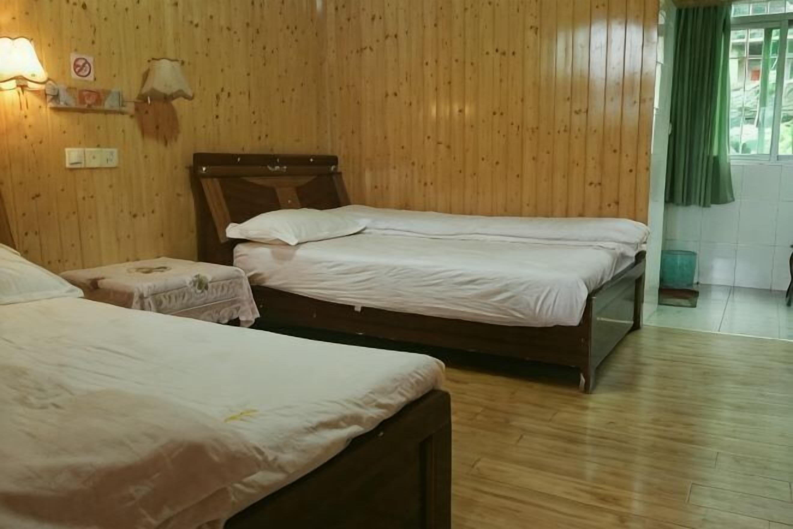 A room with two wooden beds, a nightstand, a lamp, and a window with curtains.