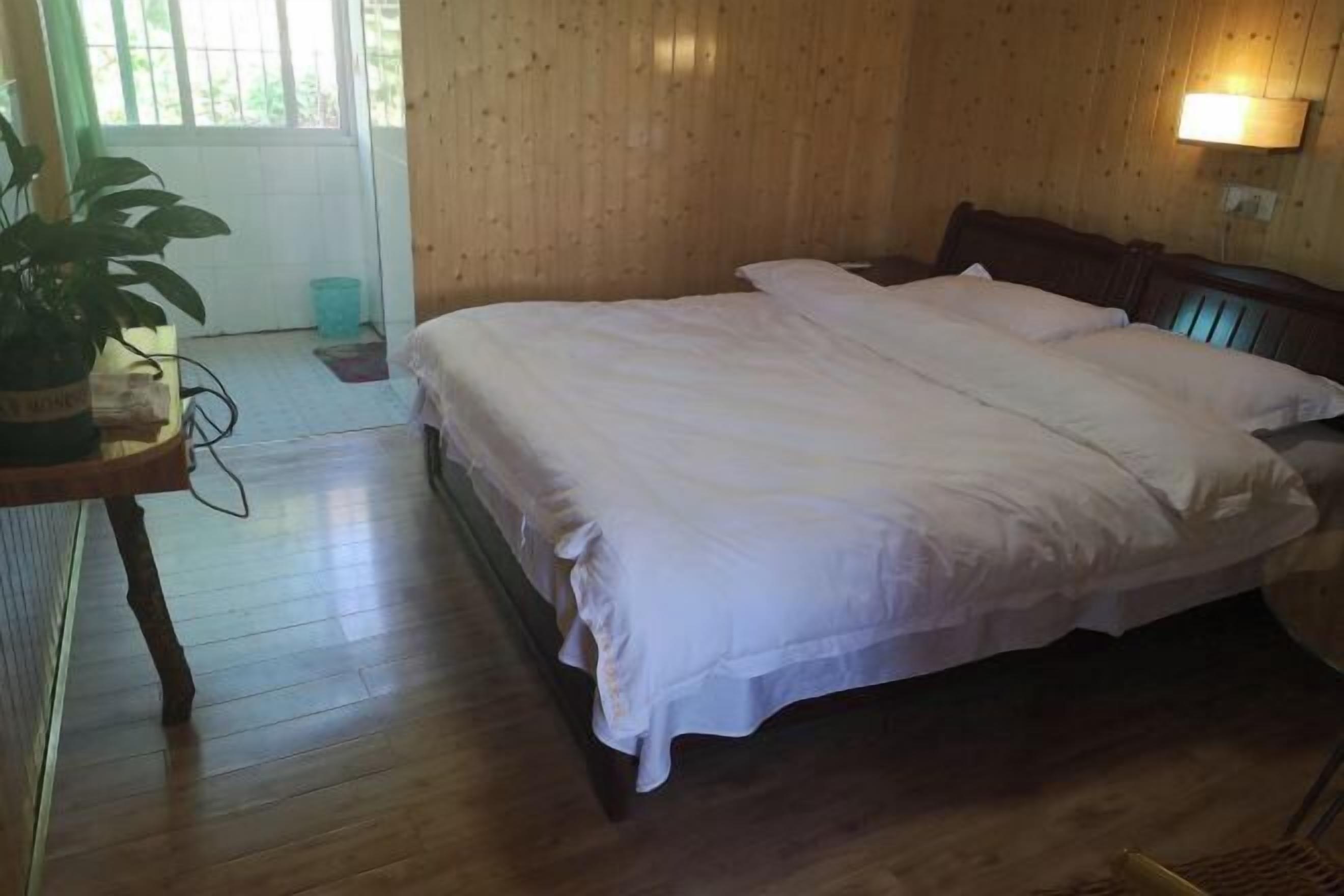 Una habitación con paneles de madera, una cama, una mesita con una planta y una ventana con vistas.