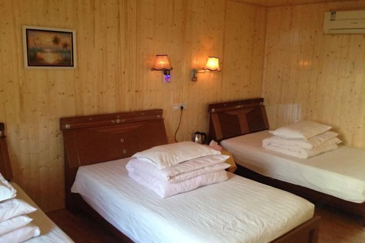A room with two wooden beds, each with white linens and pillows, and two wall-mounted lamps.
