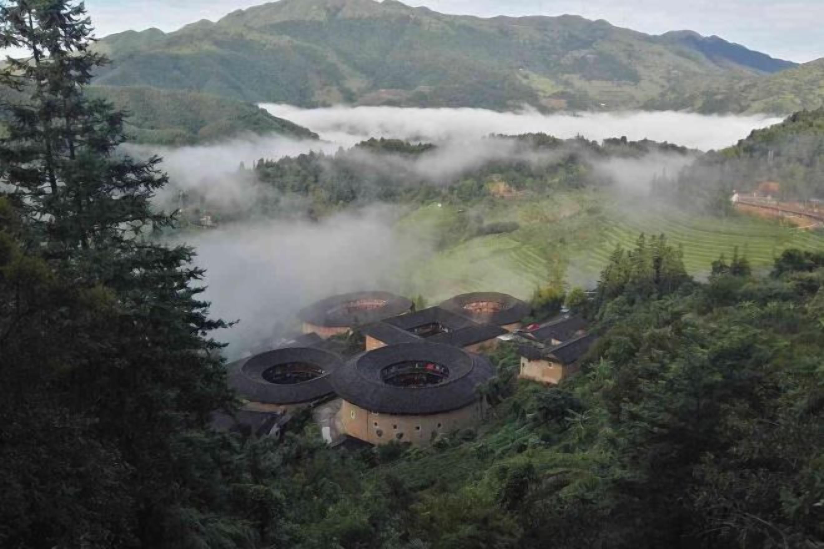 Un paisaje montañoso con edificaciones de techo curvo tradicional, rodeado de un bosque denso y bruma.