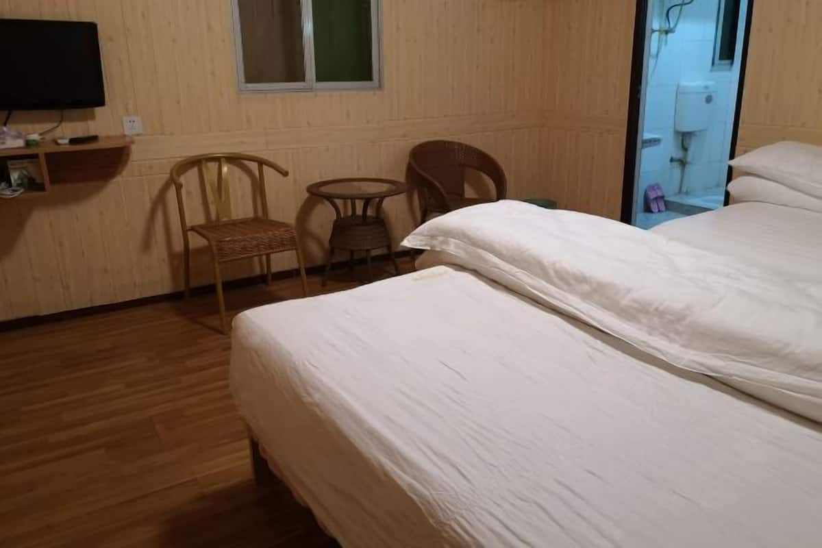 A hotel room with a wooden floor, a bed with white bedding, two wicker chairs, a small round table, and a TV on a shelf.