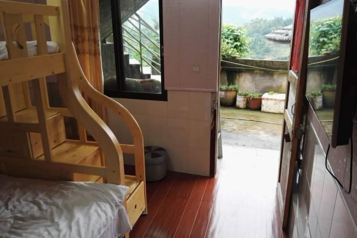 A room with a wooden bunk bed, a small window, and a view of a garden and mountains.